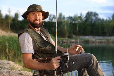 Photo of Fisherman with rod sitting on chair near lake at summer