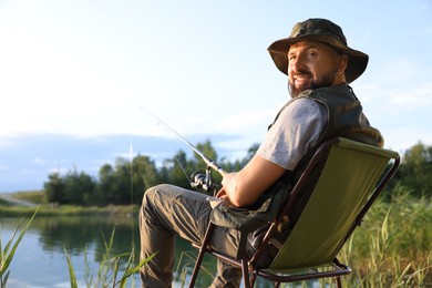 Photo of Fisherman with rod sitting on chair and fishing near lake at summer