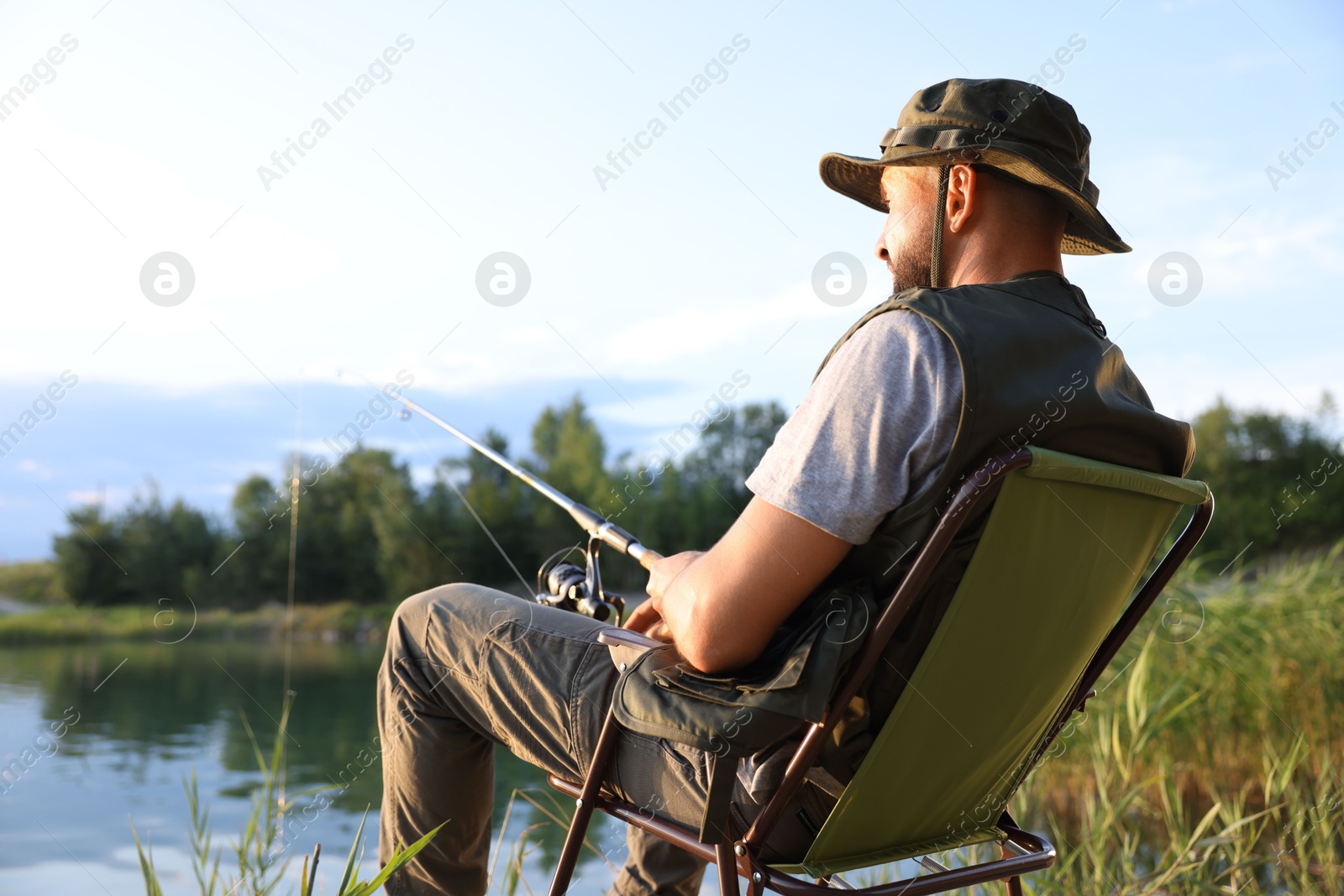Fisherman with rod sitting on chair and fishing near lake at summer Photo of Fisherman with rod sitting on chair and fishing near lake at summer