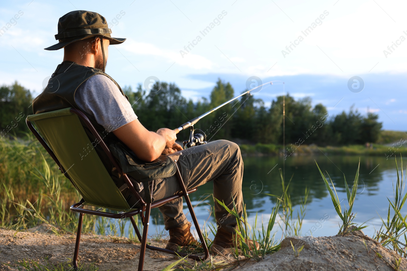 Fisherman with rod sitting on chair and fishing near lake at summer Photo of Fisherman with rod sitting on chair and fishing near lake at summer