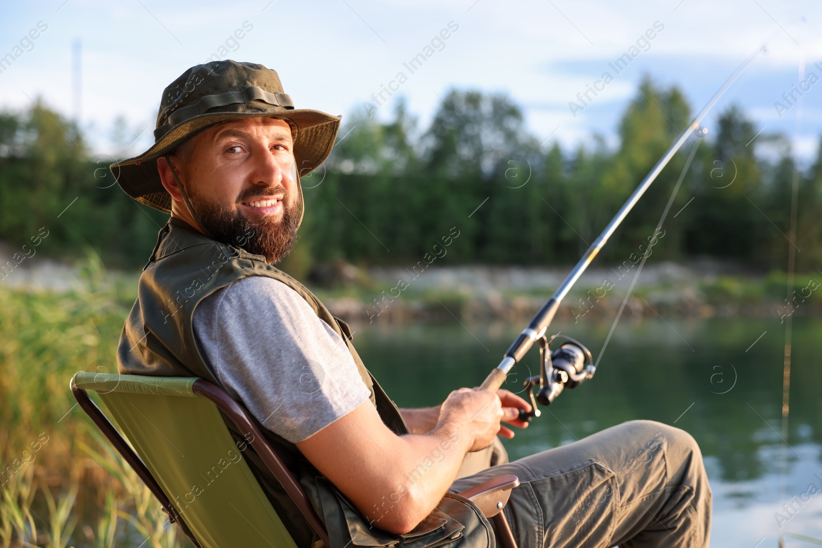 Fisherman with rod sitting on chair and fishing near lake at summer Photo of Fisherman with rod sitting on chair and fishing near lake at summer
