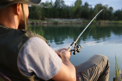 Photo of Fisherman with rod fishing near lake at summer, selective focus