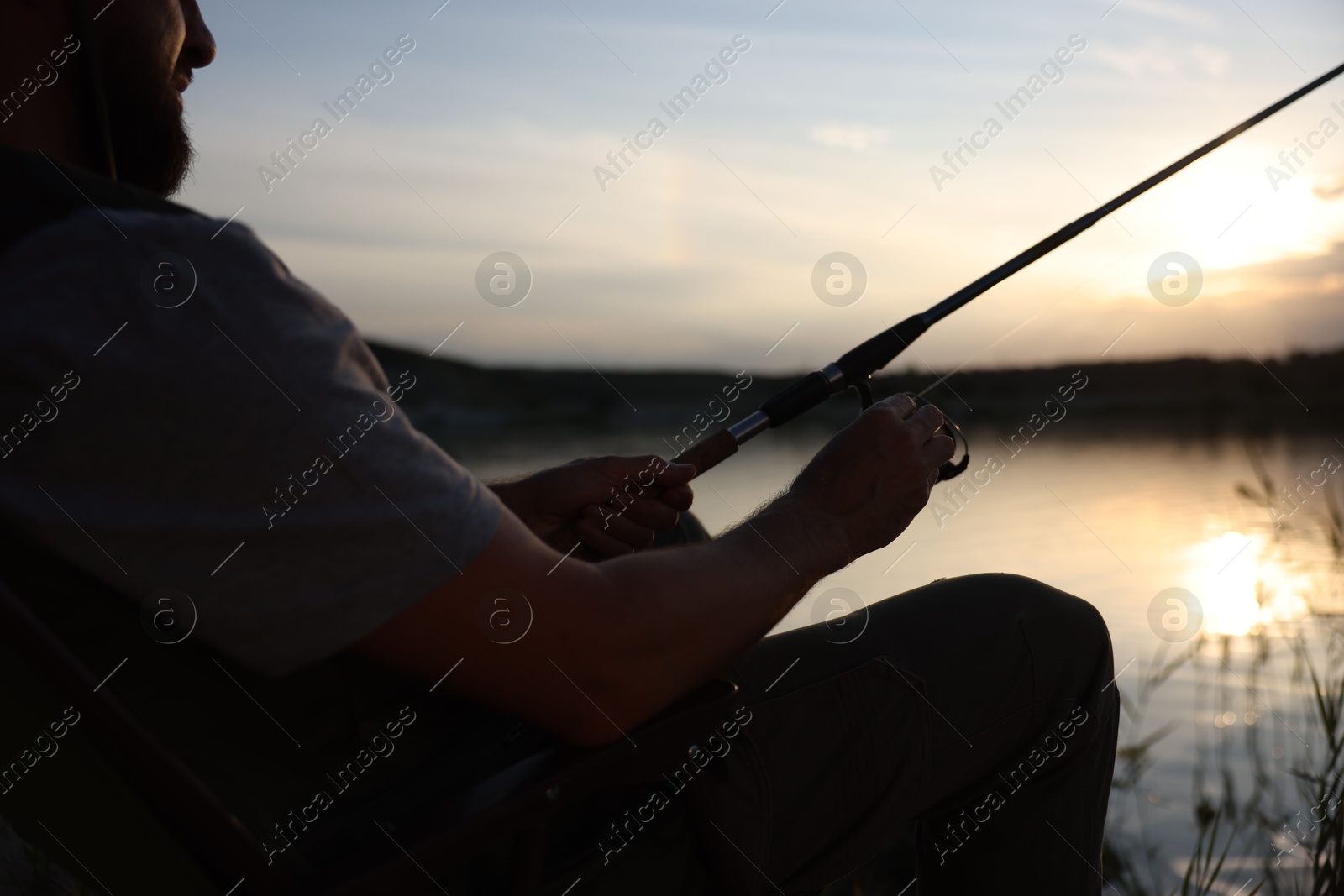 Fisherman with rod fishing near lake at sunset, closeup Photo of Fisherman with rod fishing near lake at sunset, closeup