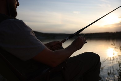 Photo of Fisherman with rod fishing near lake at sunset, closeup
