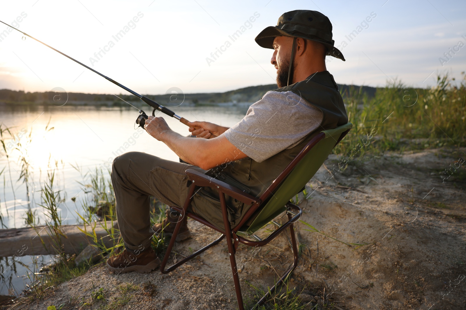 Fisherman with rod sitting on chair and fishing near lake at summer Photo of Fisherman with rod sitting on chair and fishing near lake at summer