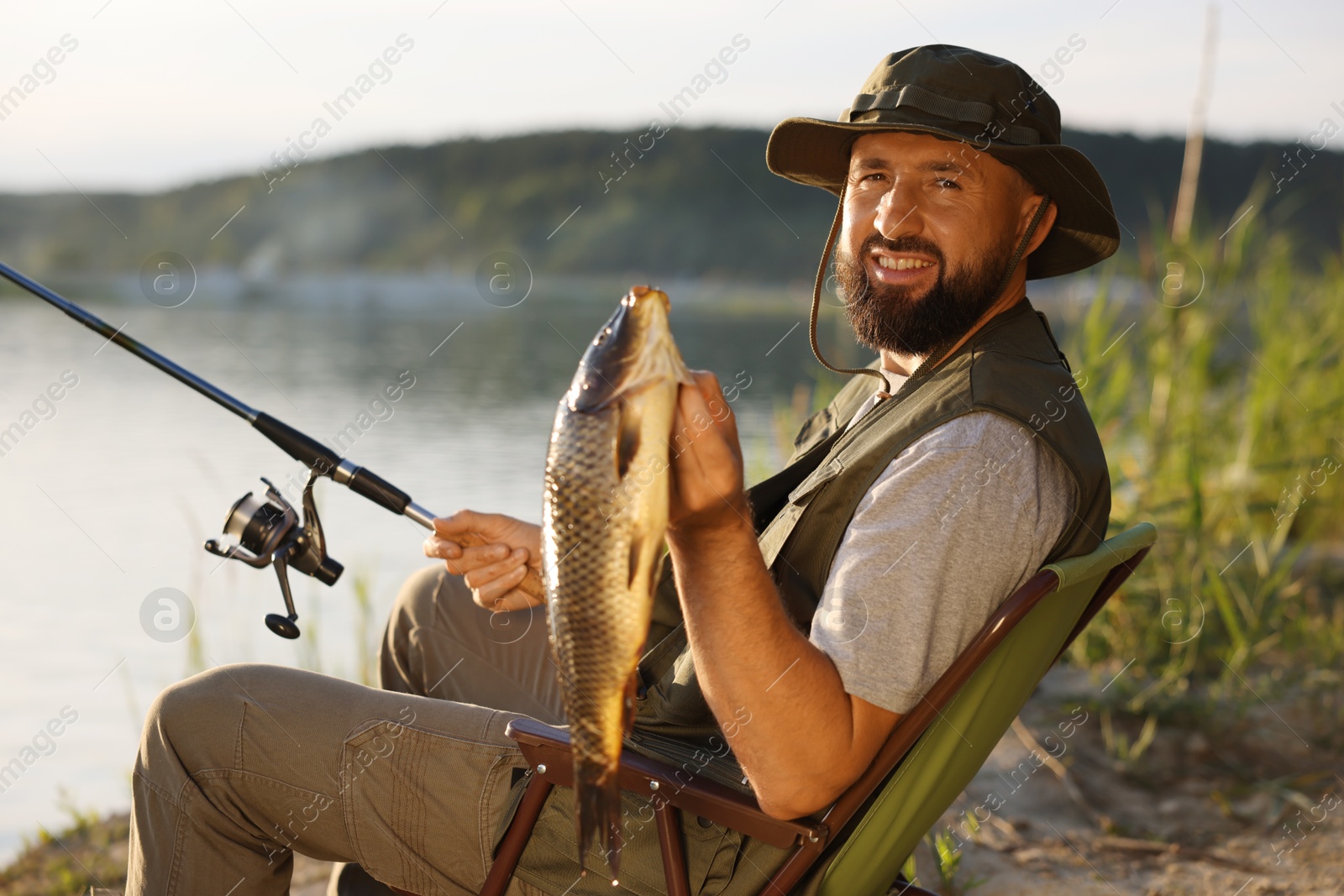 Smiling fisherman holding rod and caught fish near lake at summer Photo of Smiling fisherman holding rod and caught fish near lake at summer