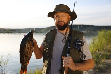 Photo of Fisherman holding rod and caught fish near lake at summer