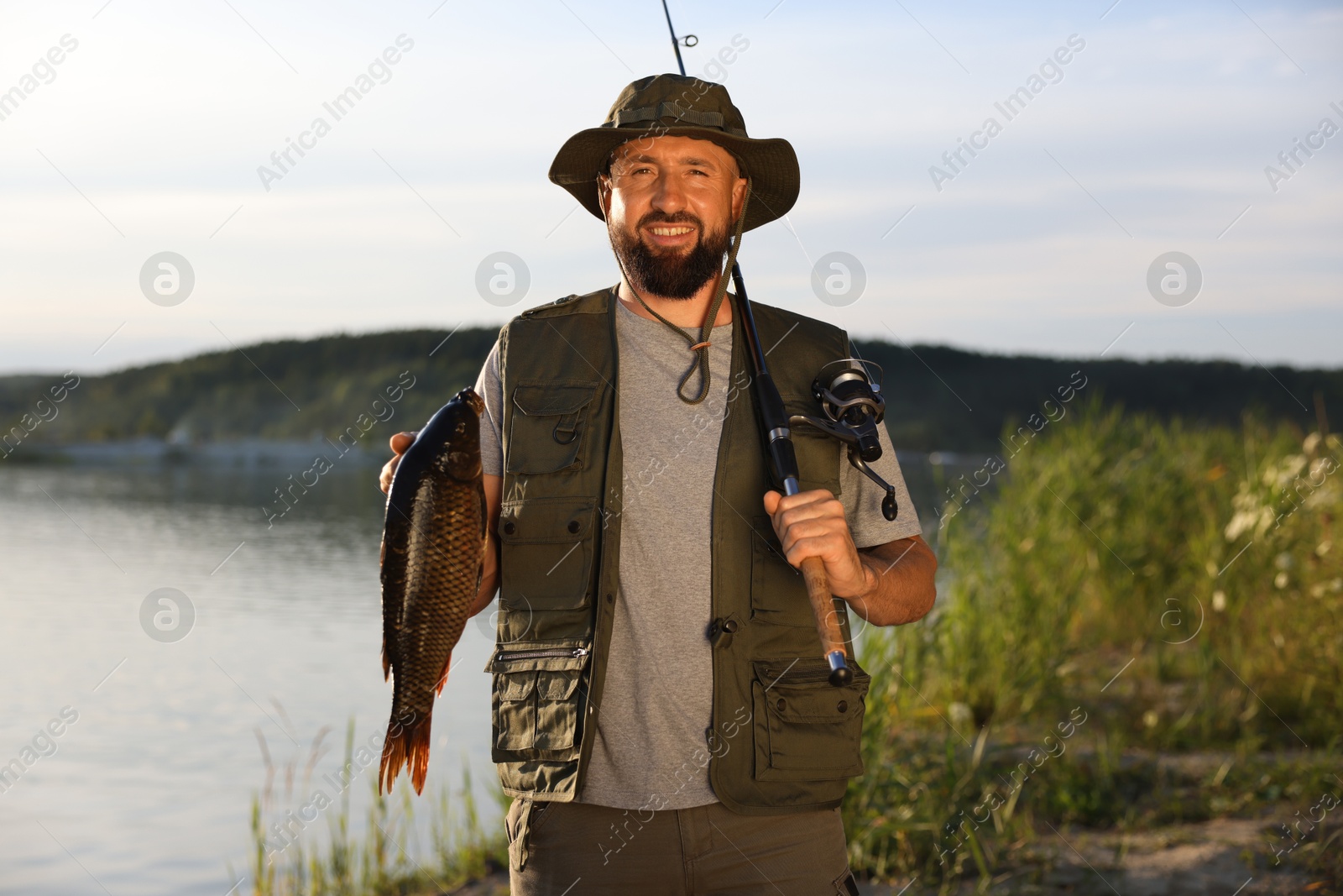 Smiling fisherman holding rod and caught fish near lake at summer Photo of Smiling fisherman holding rod and caught fish near lake at summer