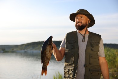 Photo of Smiling fisherman holding caught fish near lake at summer