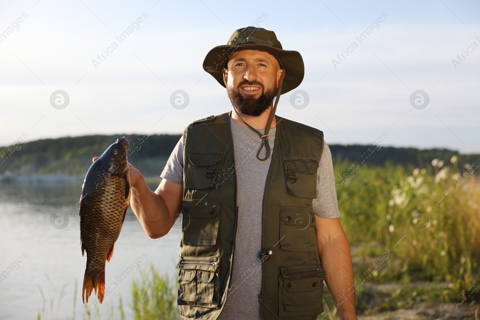 Smiling fisherman holding caught fish near lake at summer Photo of Smiling fisherman holding caught fish near lake at summer