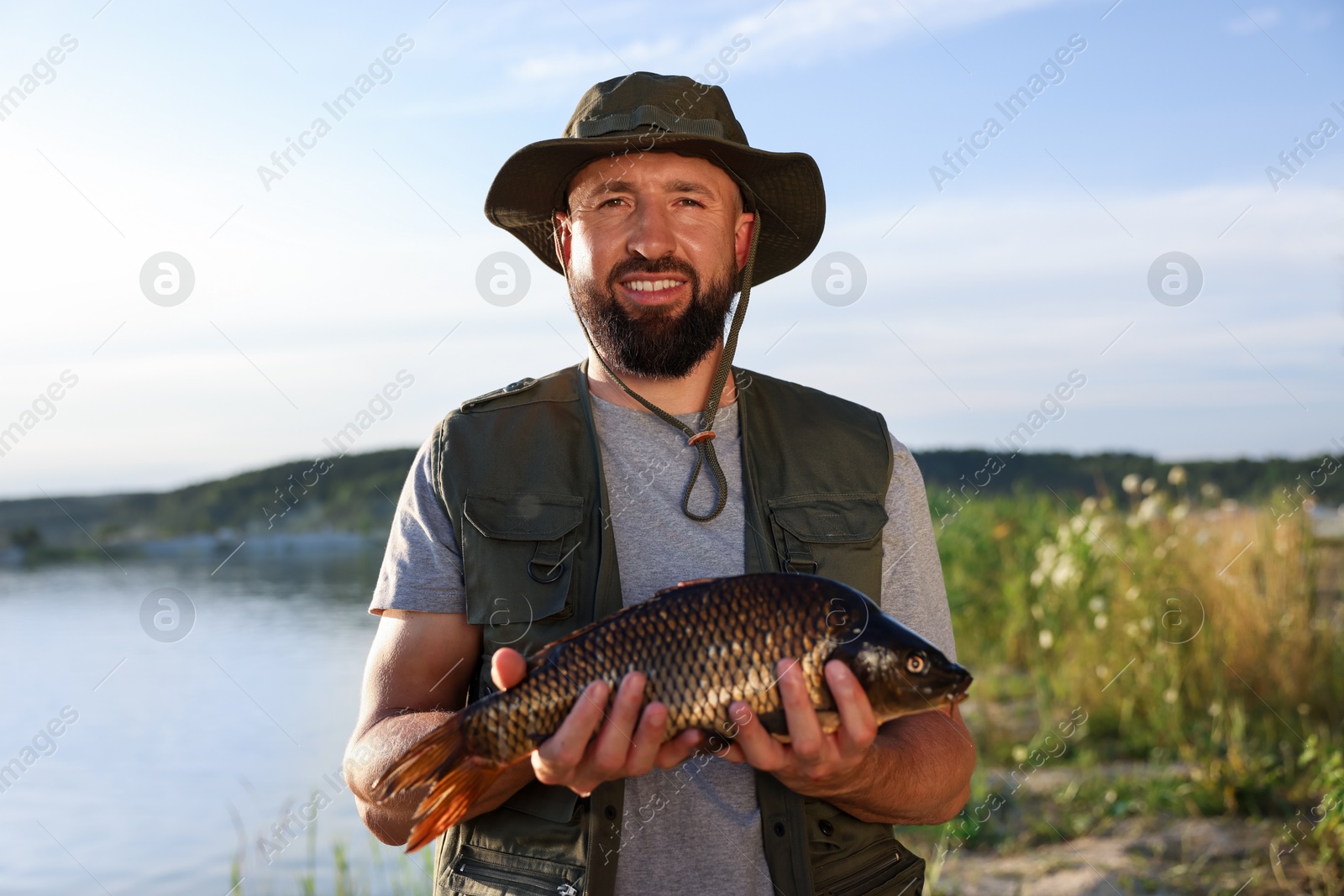 Smiling fisherman holding caught fish near lake at summer Photo of Smiling fisherman holding caught fish near lake at summer