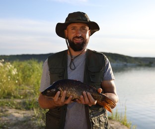 Photo of Smiling fisherman holding caught fish near lake at summer