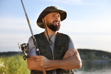 Photo of Smiling fisherman with rod near lake at summer