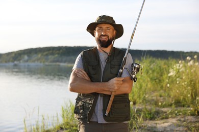 Photo of Smiling fisherman with rod near lake at summer