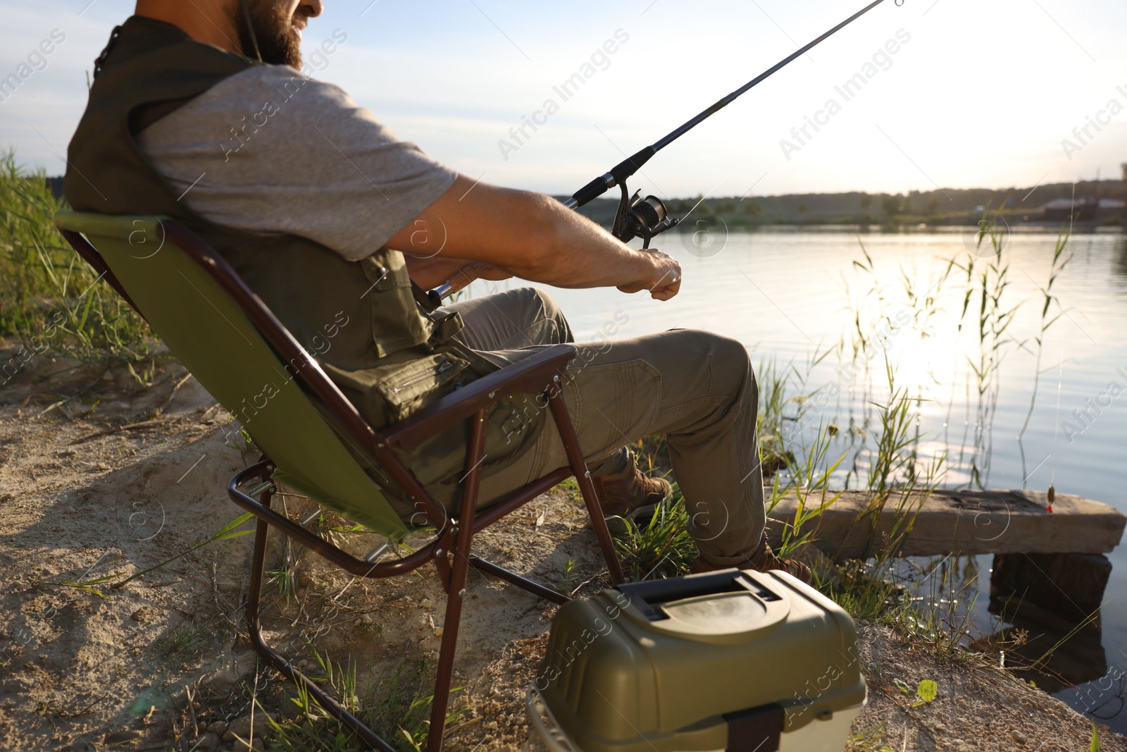 Fisherman with rod sitting on chair and fishing near lake at summer, closeup Photo of Fisherman with rod sitting on chair and fishing near lake at summer, closeup
