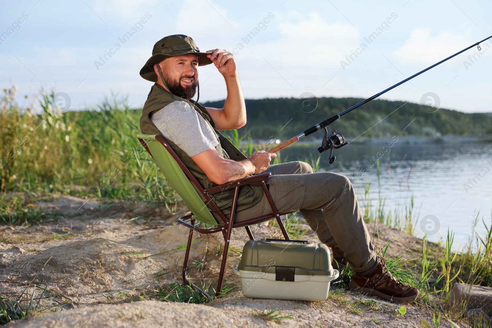 Fisherman with rod sitting on chair and fishing near lake at summer Photo of Fisherman with rod sitting on chair and fishing near lake at summer