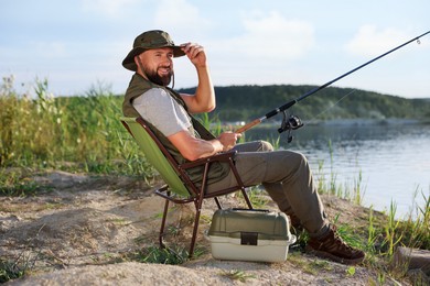 Photo of Fisherman with rod sitting on chair and fishing near lake at summer