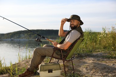 Photo of Fisherman with rod sitting on chair and fishing near lake at summer