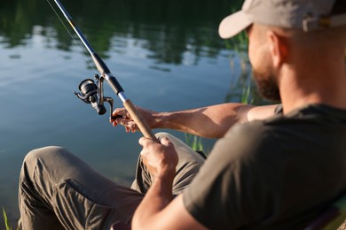 Photo of Fisherman with rod fishing near lake at summer, selective focus