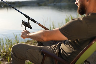 Photo of Fisherman with rod sitting on chair and fishing near lake at summer, closeup