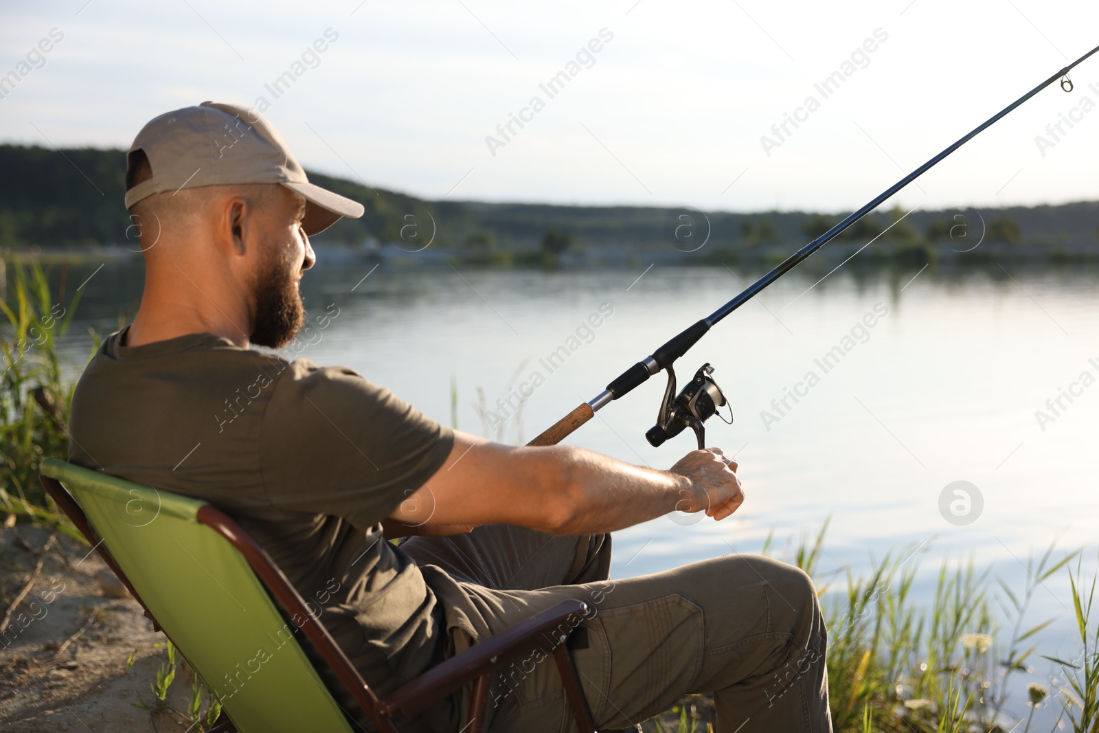 Fisherman with rod sitting on chair and fishing near lake at summer Photo of Fisherman with rod sitting on chair and fishing near lake at summer