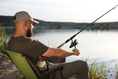 Photo of Fisherman with rod sitting on chair and fishing near lake at summer