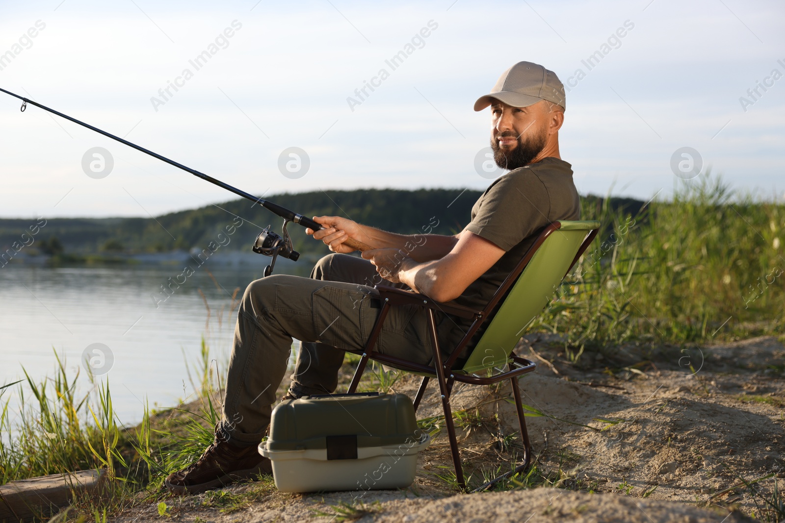 Fisherman with rod sitting on chair and fishing near lake at summer Photo of Fisherman with rod sitting on chair and fishing near lake at summer