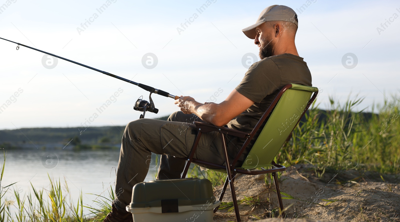 Fisherman with rod sitting on chair and fishing near lake at summer Photo of Fisherman with rod sitting on chair and fishing near lake at summer