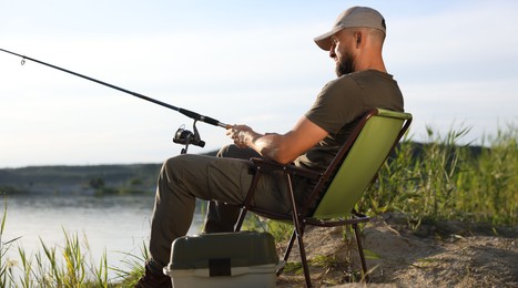 Photo of Fisherman with rod sitting on chair and fishing near lake at summer