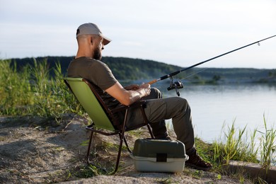 Photo of Fisherman with rod sitting on chair and fishing near lake at summer