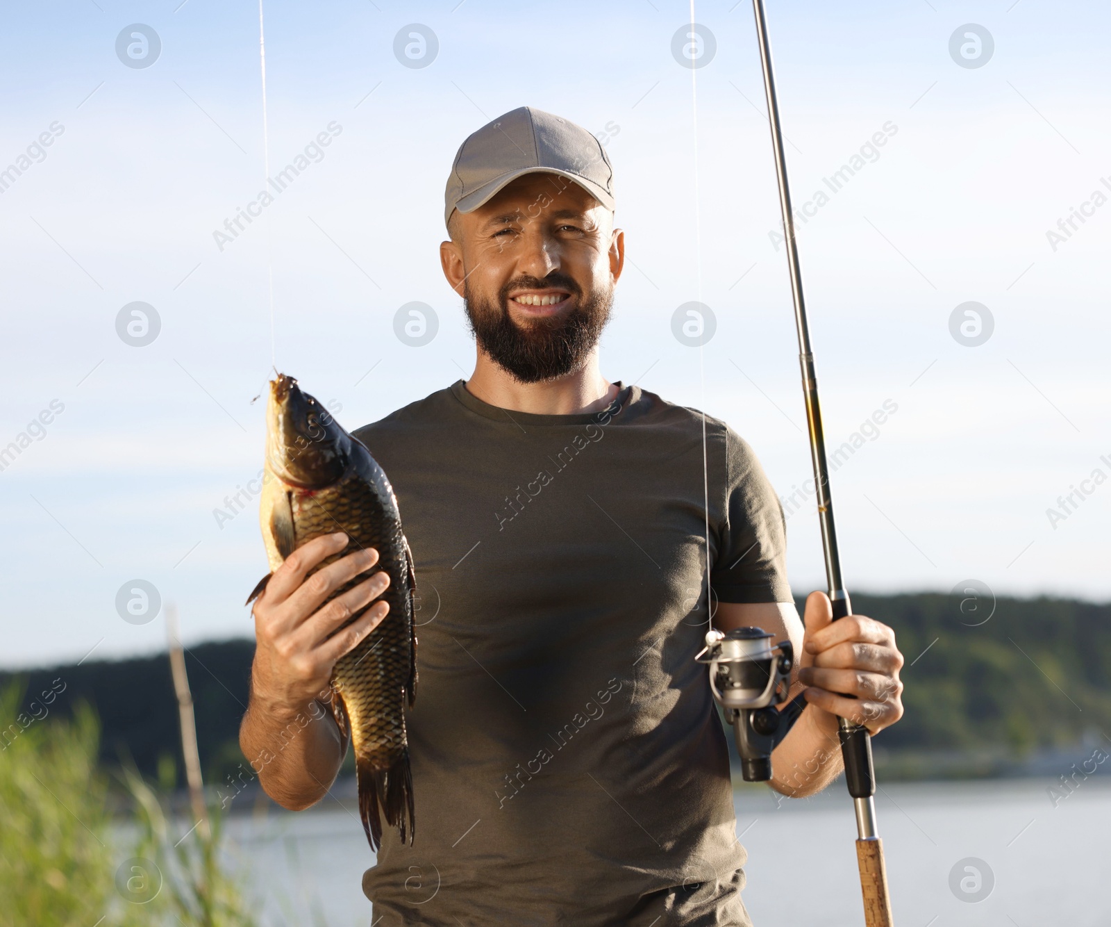 Smiling fisherman holding rod and caught fish near lake at summer Photo of Smiling fisherman holding rod and caught fish near lake at summer