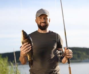 Photo of Smiling fisherman holding rod and caught fish near lake at summer