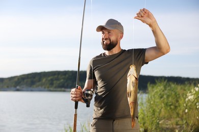Photo of Smiling fisherman holding rod and caught fish near lake at summer