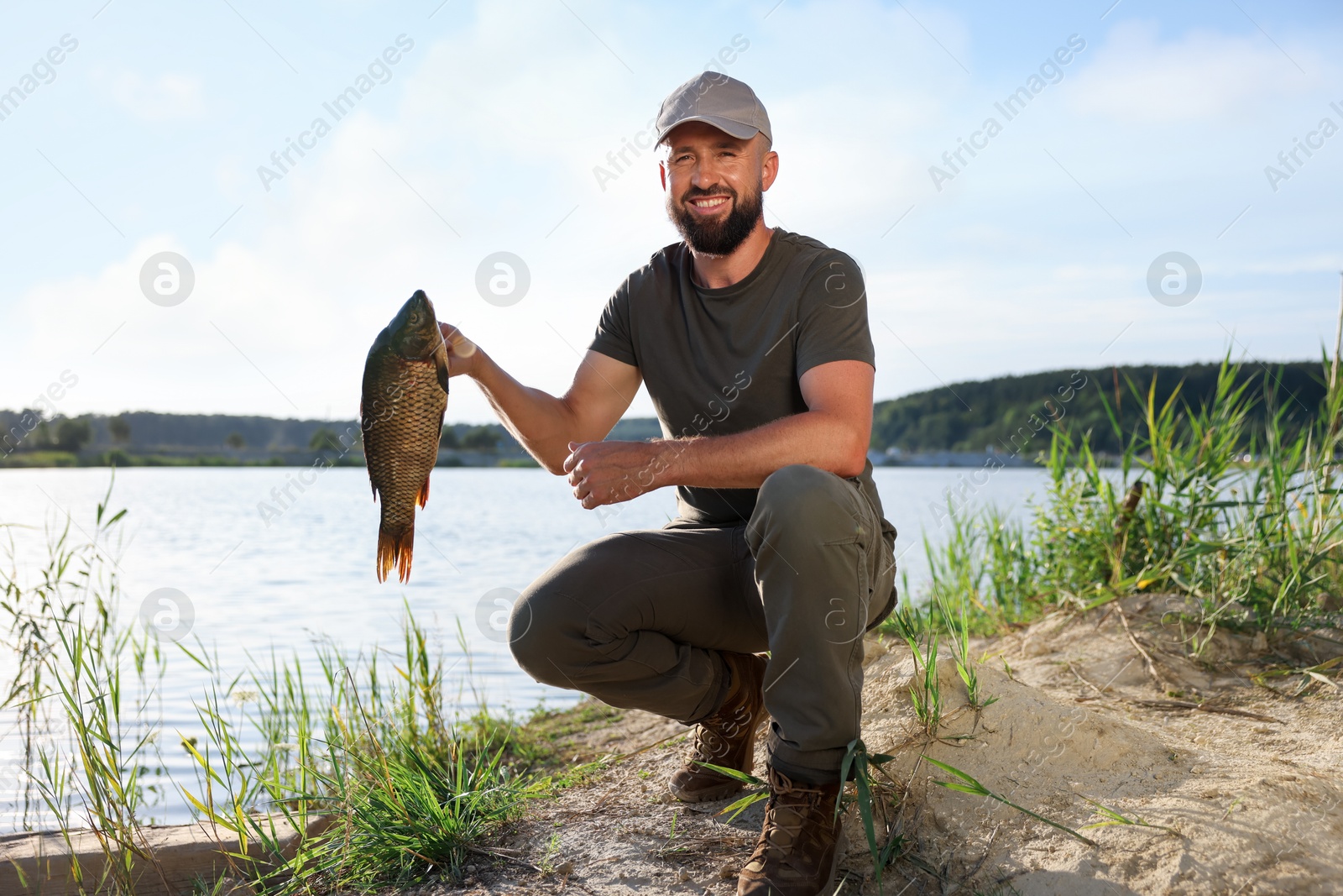 Smiling fisherman holding caught fish near lake at summer Photo of Smiling fisherman holding caught fish near lake at summer