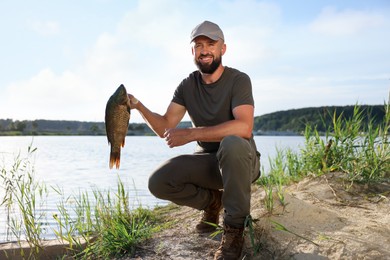 Photo of Smiling fisherman holding caught fish near lake at summer
