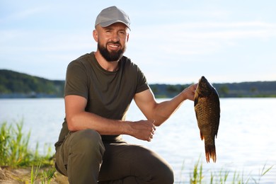 Photo of Smiling fisherman holding caught fish near lake at summer