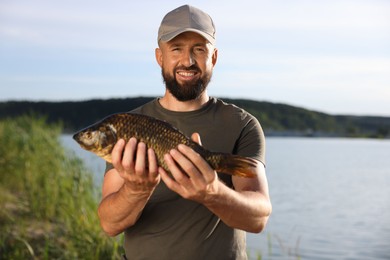 Photo of Smiling fisherman holding caught fish near lake at summer