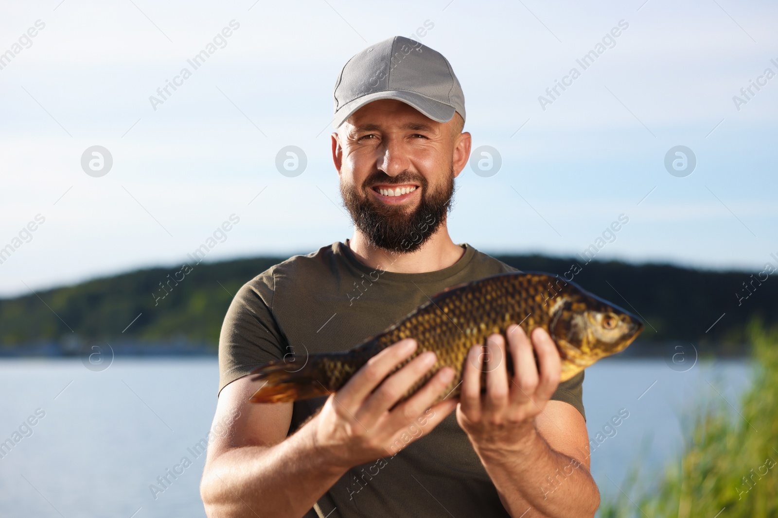 Smiling fisherman holding caught fish near lake at summer Photo of Smiling fisherman holding caught fish near lake at summer