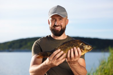 Photo of Smiling fisherman holding caught fish near lake at summer