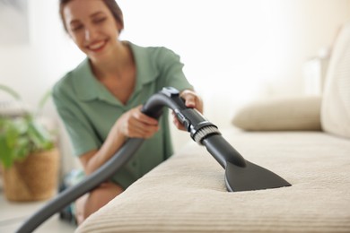 Photo of Woman cleaning sofa with vacuum cleaner at home, selective focus