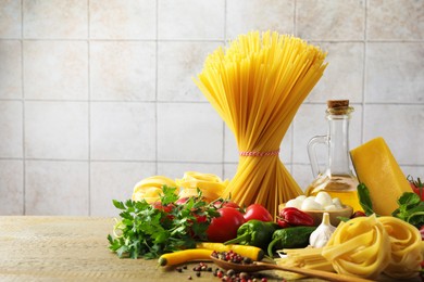 Photo of Different types of pasta and ingredients on wooden table, space for text