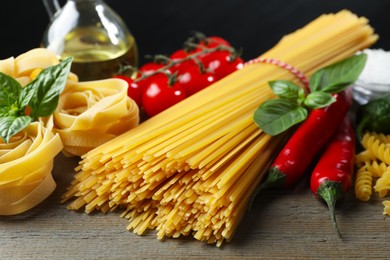 Photo of Different types of pasta and ingredients on wooden table, closeup