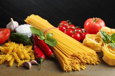 Photo of Different types of pasta and ingredients on wooden table, closeup