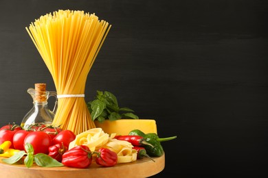 Photo of Different types of raw pasta and products on wooden board against black background, closeup. Space for text