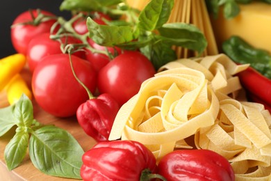 Photo of Raw tagliatelle pasta and products on wooden board, closeup