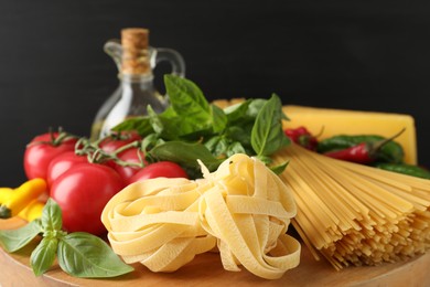 Photo of Different types of raw pasta and products on wooden board against black background, closeup