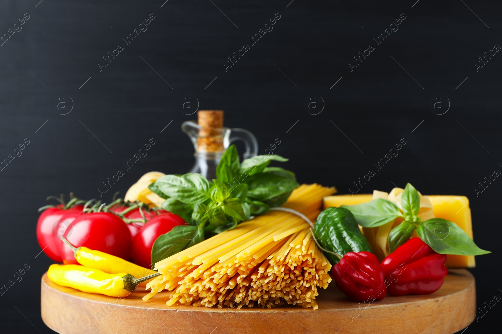 Photo of Raw spaghetti pasta and products on wooden board against black background, closeup