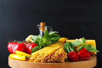 Photo of Raw spaghetti pasta and products on wooden board against black background, closeup