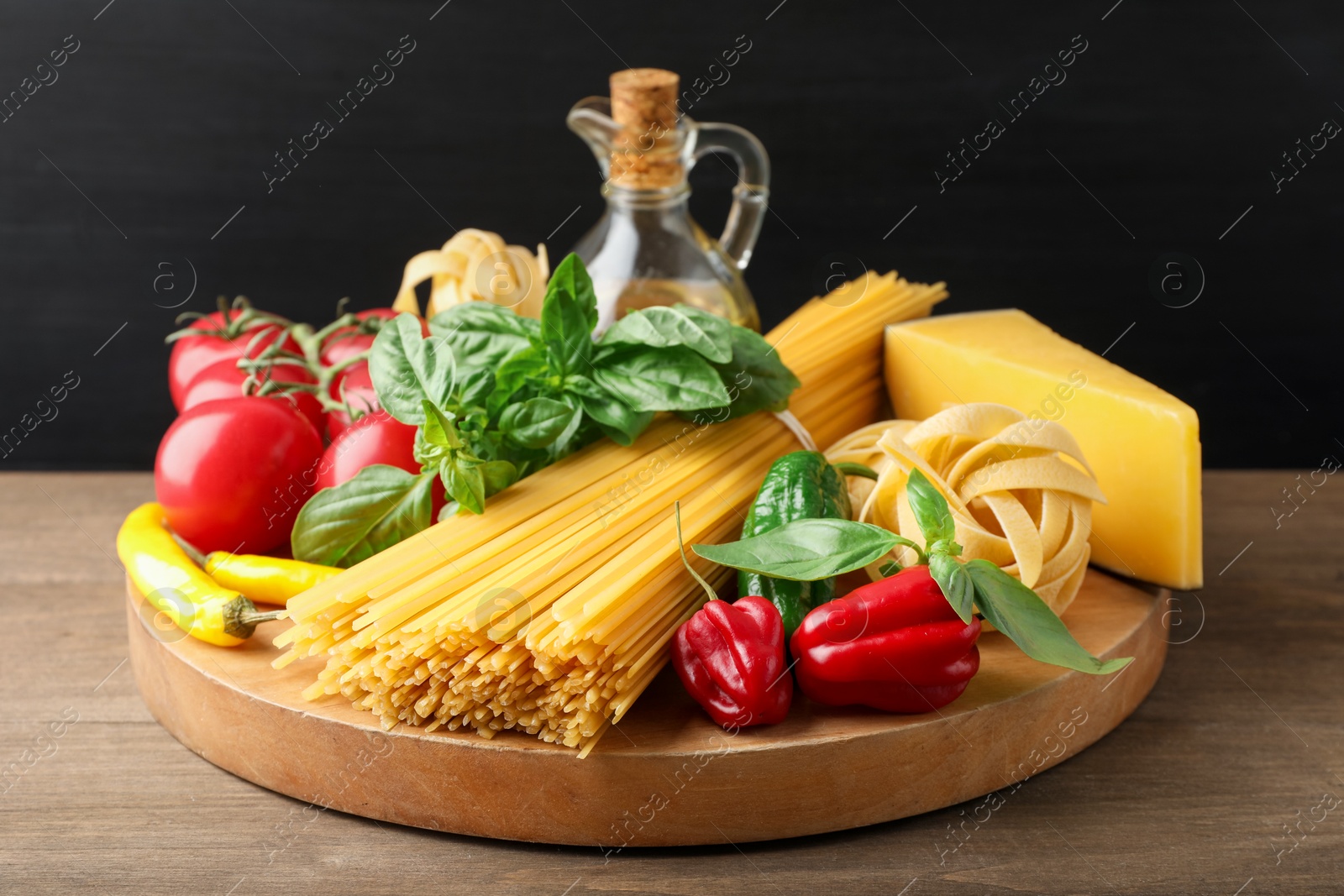 Photo of Different types of raw pasta and products on wooden table against black background, closeup