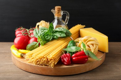 Photo of Different types of raw pasta and products on wooden table against black background, closeup